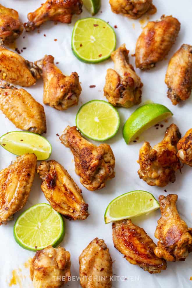 overhead shot of chili rubbed chicken wings with sliced limes on a white background.