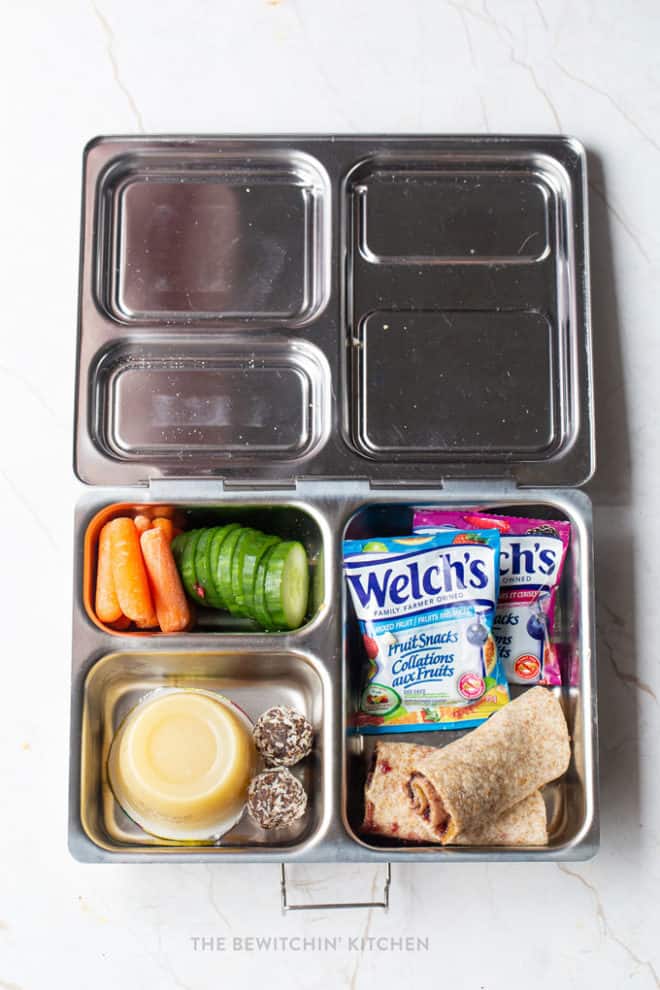 Easy school lunch idea 6 - Planet Box bento box with carrots, cucumbers, fruit snacks, apple sauce, and sun butter and jam wrap.