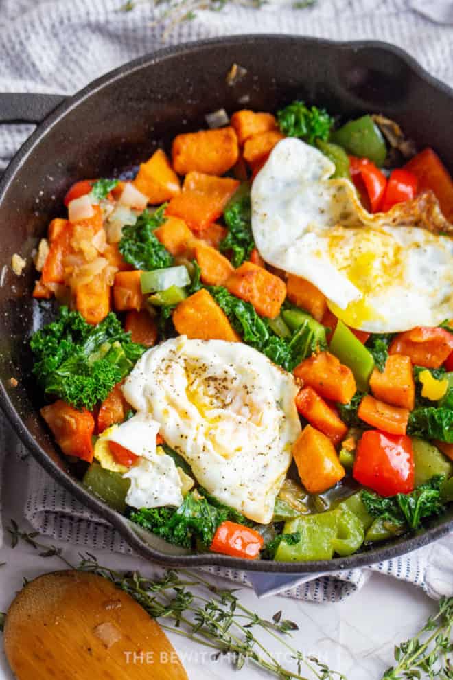 close up of egg cooked over medium in a cast iron skillet with sweet potatoes, kale, and peppers