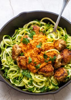 A fork twirling zucchini noodles with ground chicken meatballs and romesco sauce