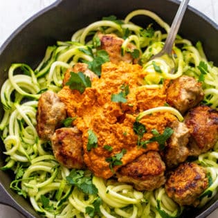 A fork twirling zucchini noodles with ground chicken meatballs and romesco sauce