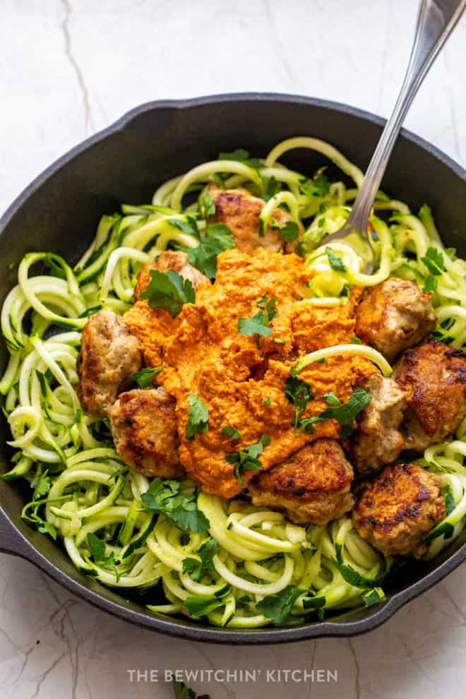 A fork twirling zucchini noodles with ground chicken meatballs and romesco sauce