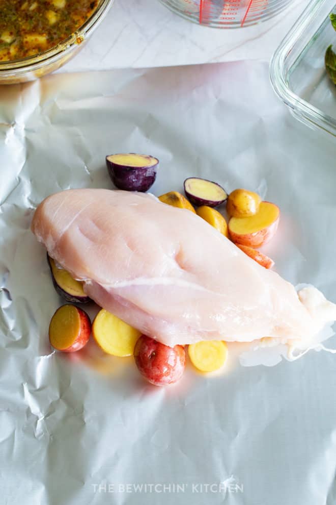 chicken laying on foil on top of potatoes ready for the grill