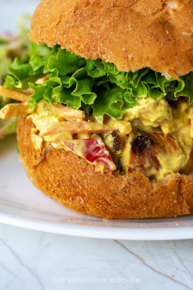 close up side view of a kaiser roll stuffed with curry mayo, chicken, raisins, and bell peppers