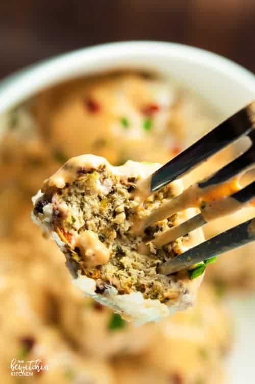 fork showing inside of a meatball over a bowl of curry meatballs