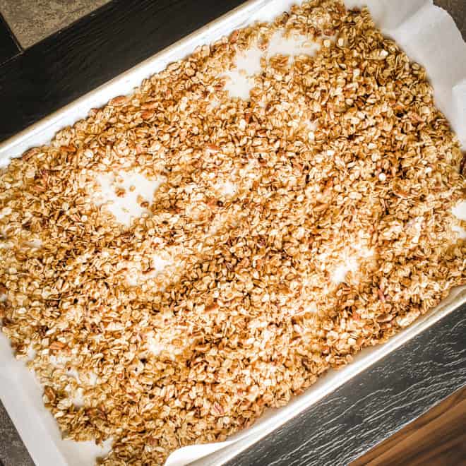 pumpkin granola spread out on a parchment lined baking sheet