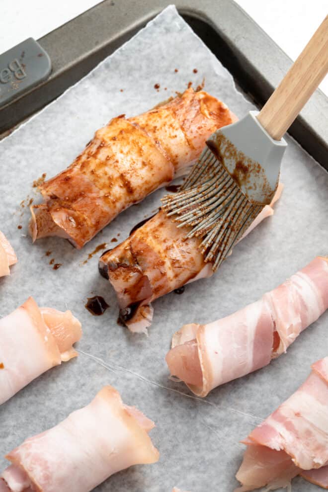 bacon wrapped chicken tenders on baking sheet with sauce