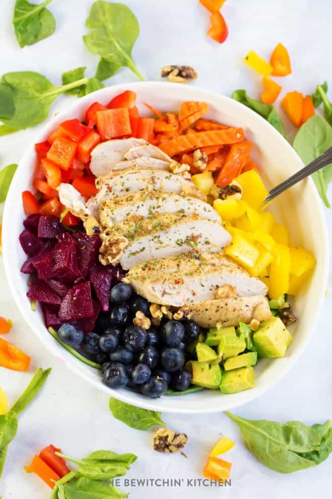 rainbow chicken salad bowl surrounded by spinach and chopped peppers