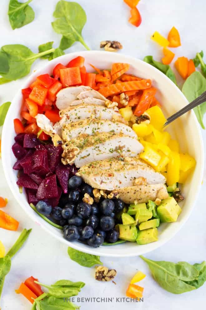 rainbow chicken salad bowl surrounded by spinach and chopped peppers