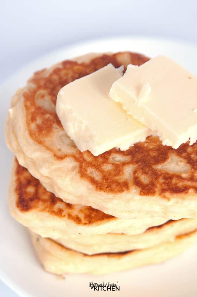 A stack of three gluten free buttermilk pancakes with two pats of butter on a white plate.