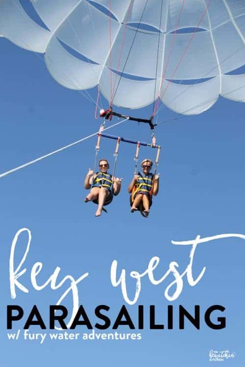 Two women parasailing against a blue sky with the words Key West Parasailing w/ fury water adventures overlaid at the bottom.