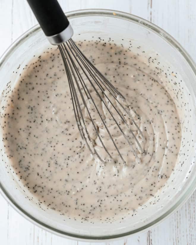 A large glass bowl filled with poppyseed cake batter and a metal whisk.
