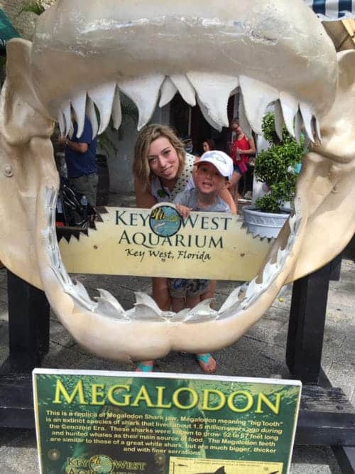 A woman and a young boy inside a reproduction of a shark's mouth. There is a small sign that reads Key West Aquarium Key West, Florida in side the mouth.