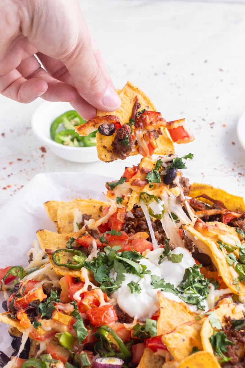 Plate of air fryer nachos topped with melted cheese, beans, and toppings, with a hand pulling a chip and melted cheese