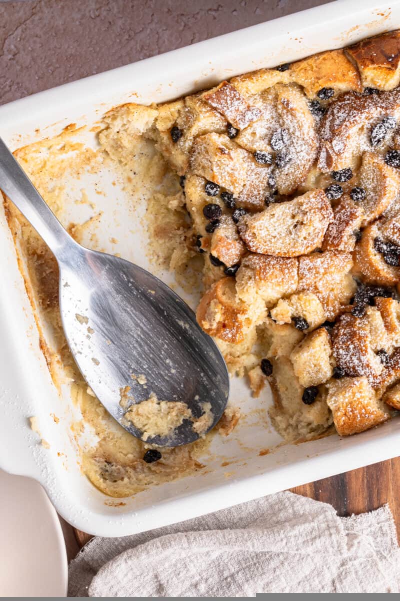Overhead of bread pudding in a baking dish with a large serving spoon and some of it missing
