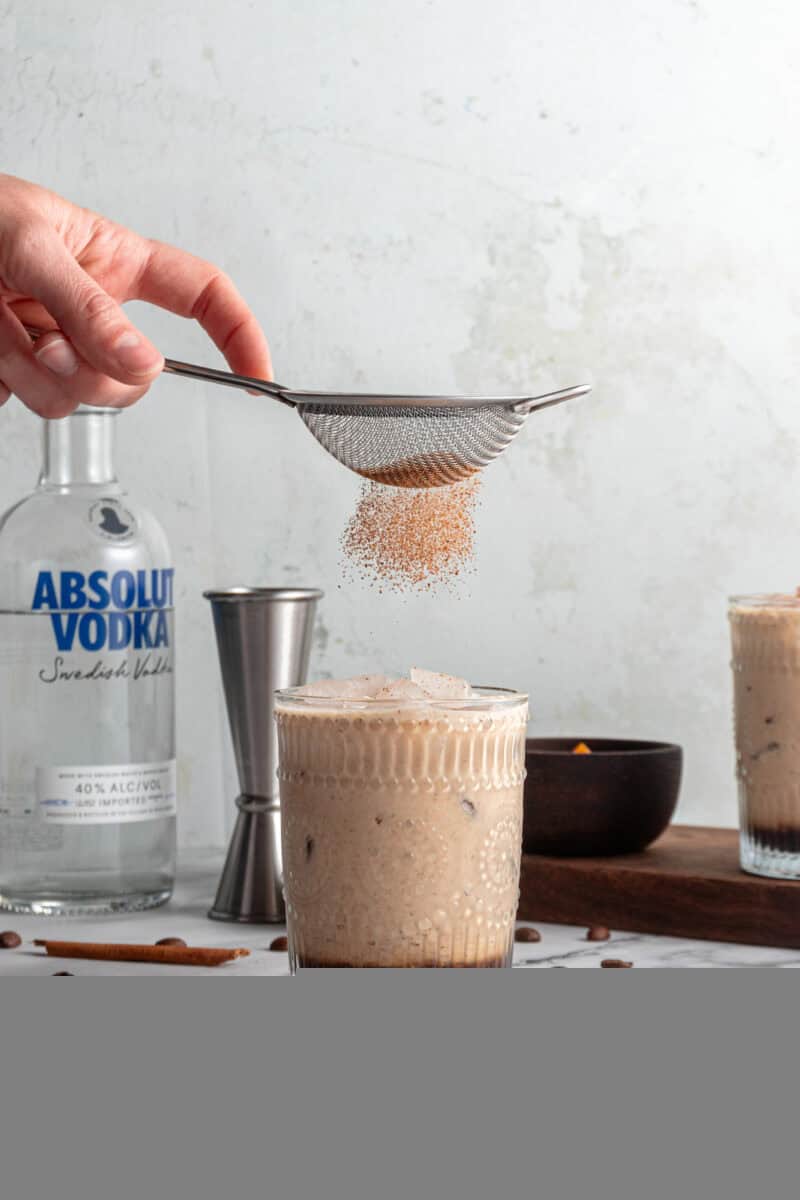 Sprinkling cinnamon onto a glass of pumpkin spice white russian